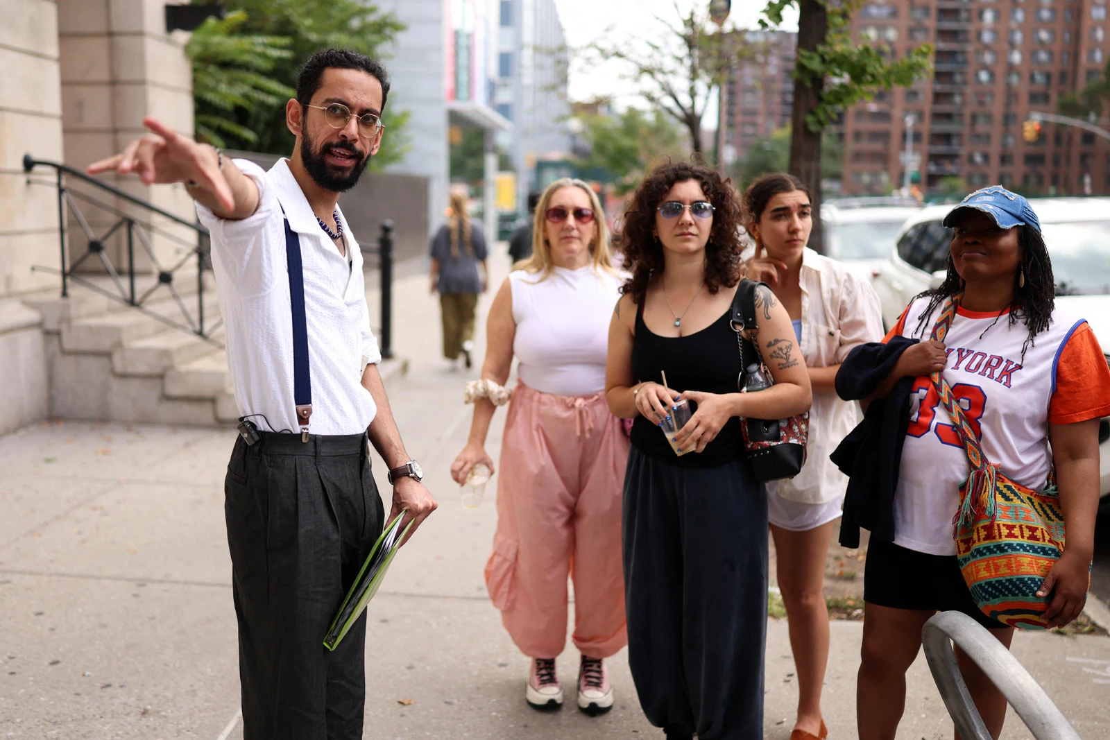 A guide pointing while standing with a group of people on a city sidewalk.