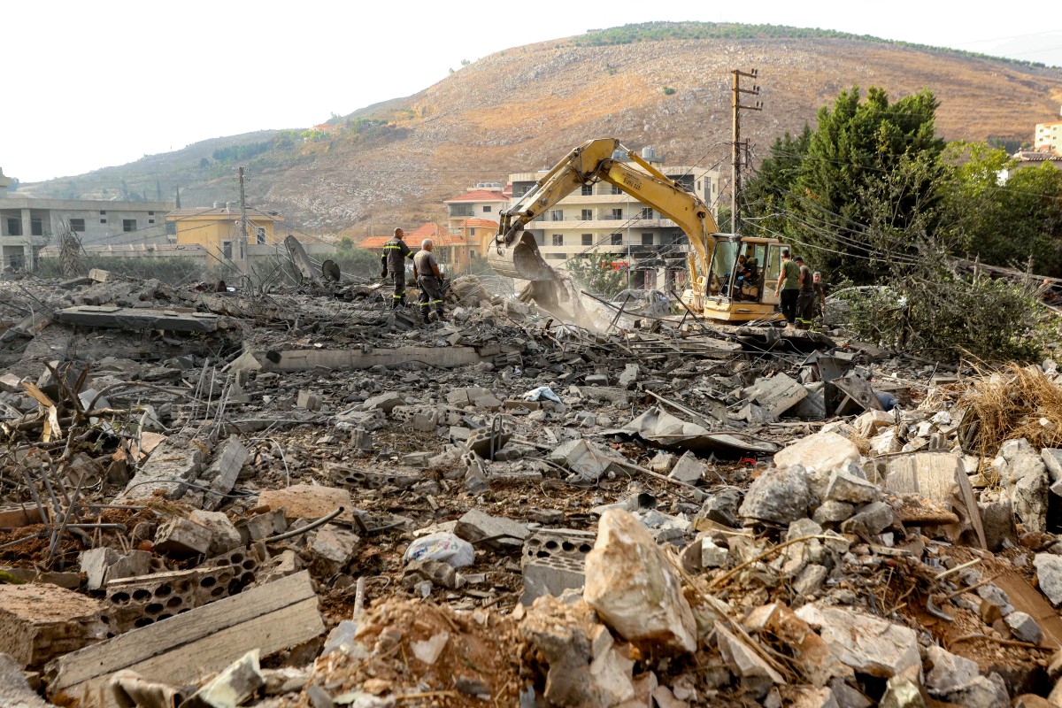 İsrail'in Kafr Rumman köyüne gece düzenlediği hava saldırısının ardından enkaz altında hayatta kalanları arayan kurtarma ekipleri, bir ekskavatörle kazı yapıyor. (AFP)