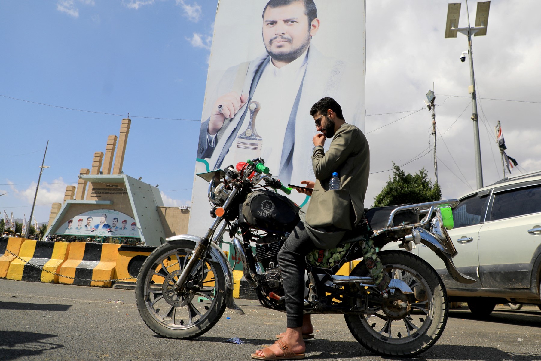 A Yemeni checks his phone above a motocycle near a portrait of Houthi leader Abdul Malik Al-Houthi, on January 18, 2024 in Sanaa. AFP/File