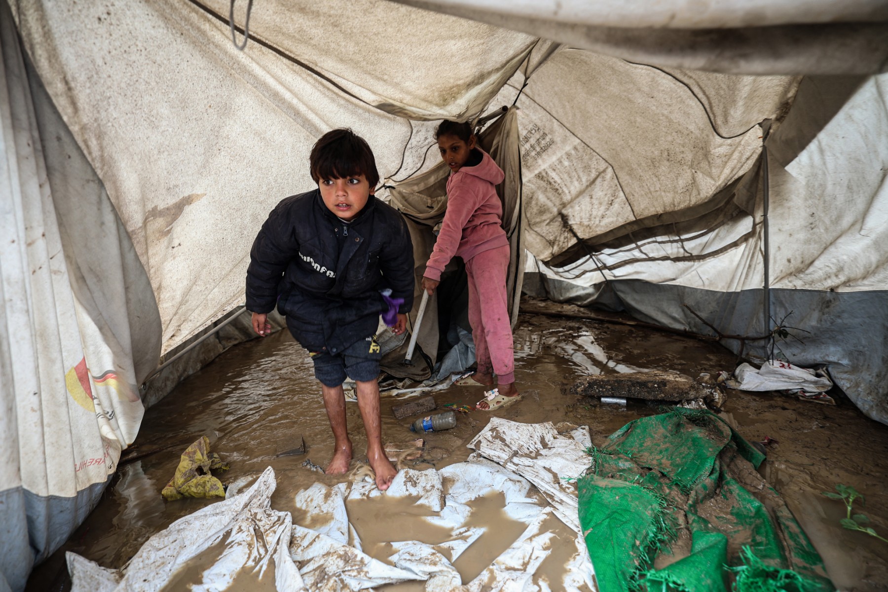 Young displaced Palestinians stand inside a tent flooded with rainwater in the Bureij refugee camp in the central Gaza Strip as the region experiences cold winter conditions on December 29, 2025. (File/AFP)