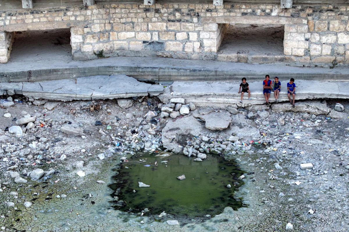 This aerial view shows children sitting by the now-dry riverbed of Syria’s Orontes (Assi) river during an extreme drought in the city of Jisr al-Shughur in Syria’s northwestern Idlib province on August 4, 2025. (AFP/File)