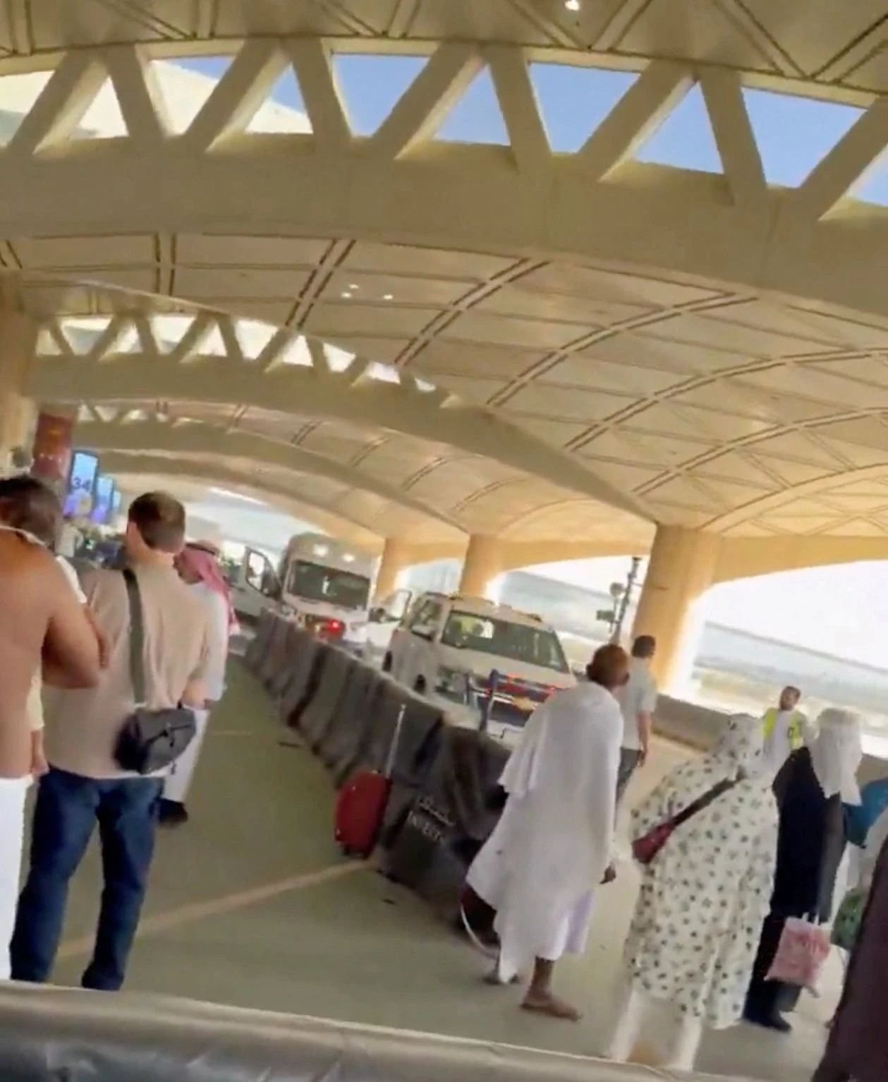 Pilgrims and travelers navigate the busy outdoor area of a modern transportation hub, with the distinctive architecture of the ceiling visible above. (AFP)