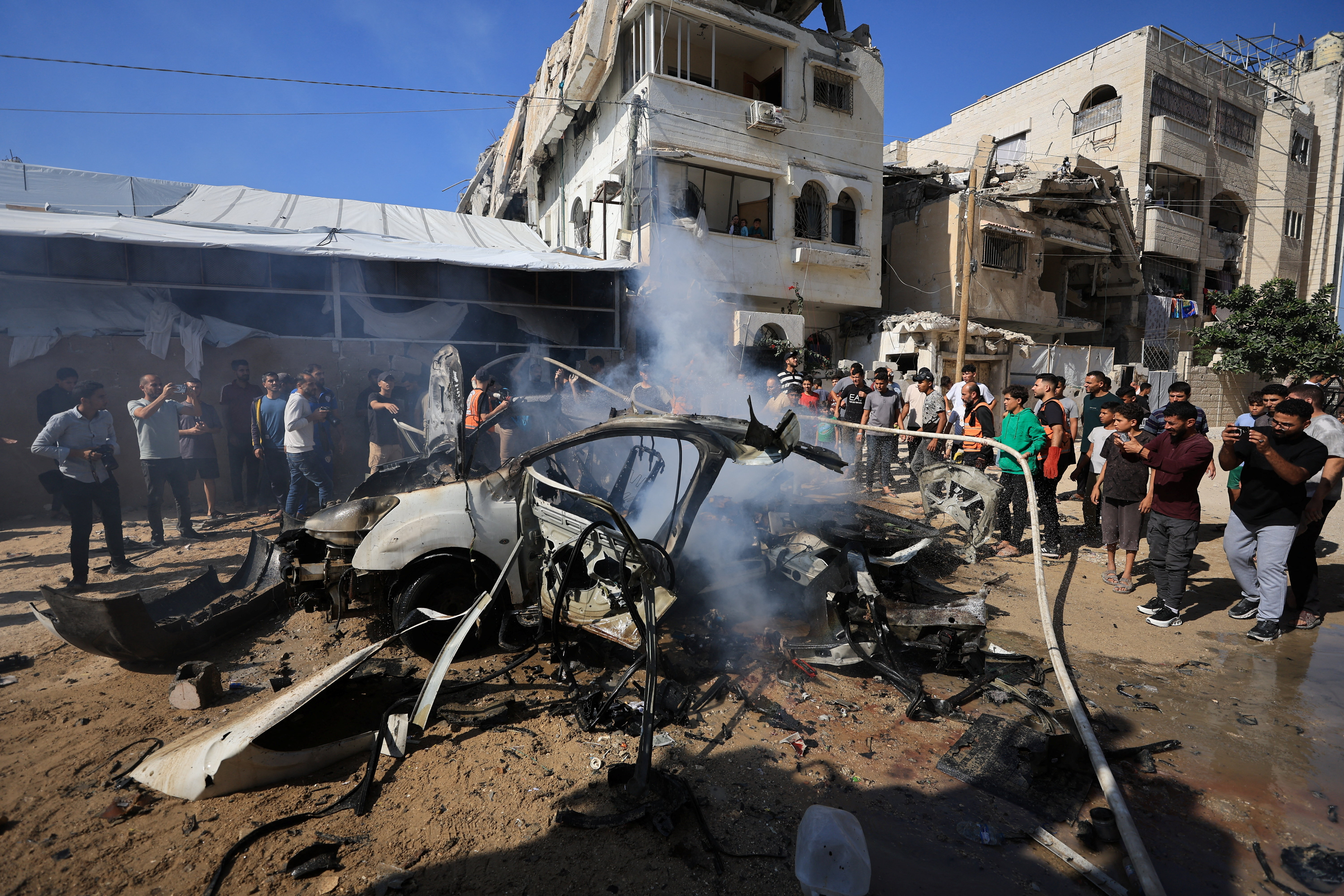 Palestinians gather around the remains of a vehicle after it was hit by an Israeli strike, according to health officials, in Gaza City, October 22, 2026. (Reuters)