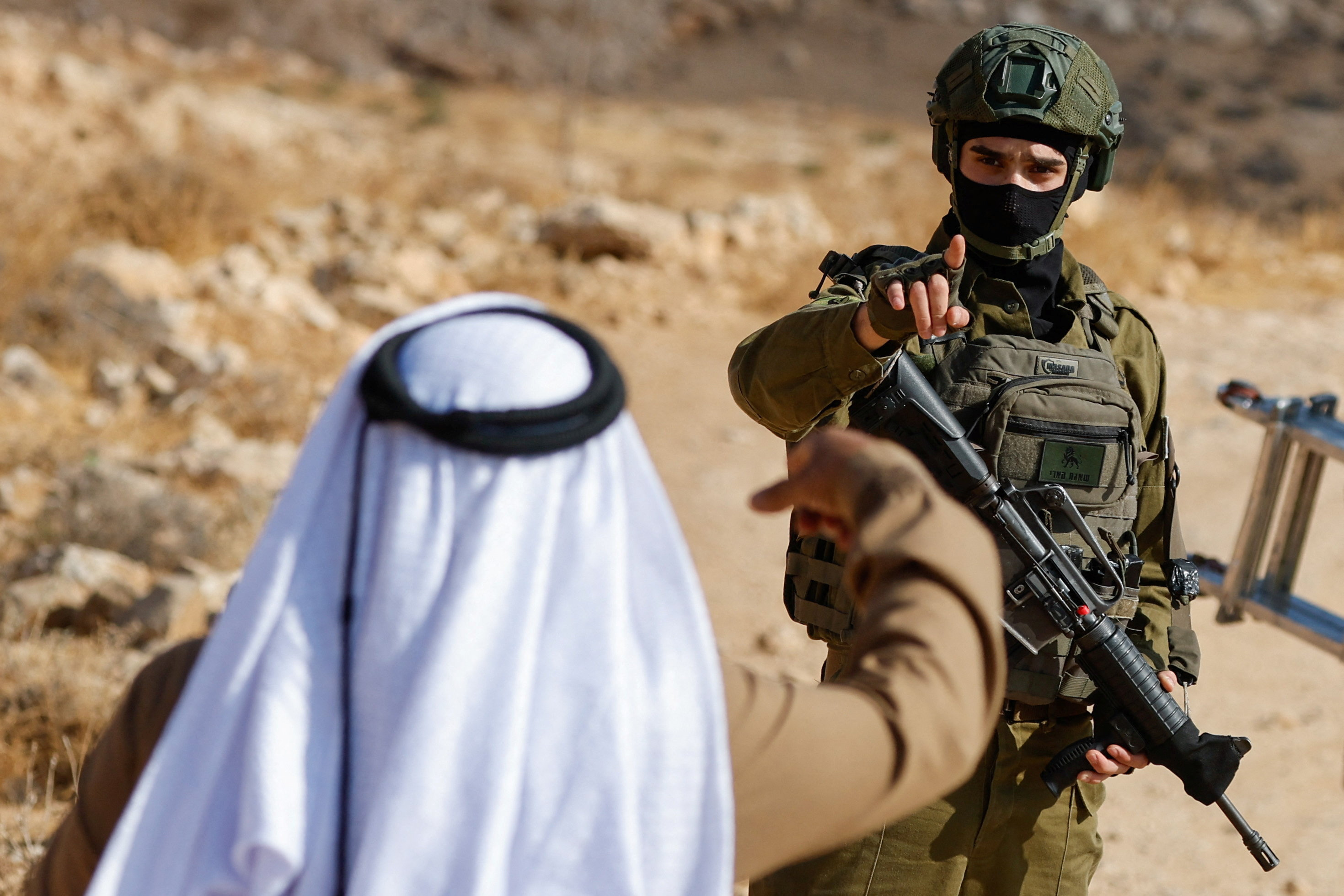 A member of the Israeli forces gestures to a Palestinian as he stands guard during the demolition of a Palestinian building near Hebron in the Israeli-occupied West Bank, October 5, 2026. (REUTERS/Mussa)