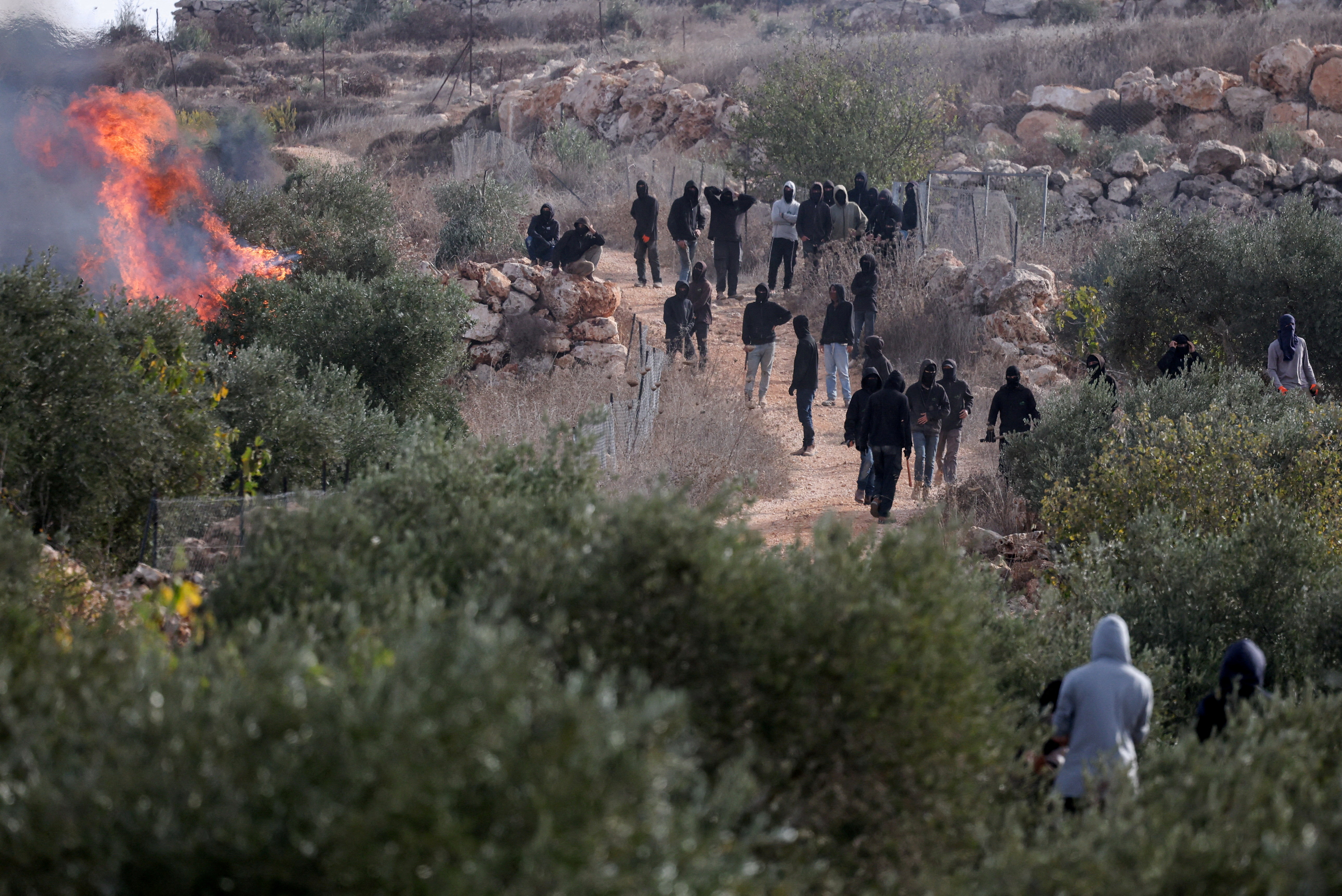 Palestinians look on as settlers stand near a fire during olive-harvest clashes in Abu Falah, near Ramallah, occupied West Bank, Oct. 16, 2026. (Reuters/Ammar Awad/File Photo)