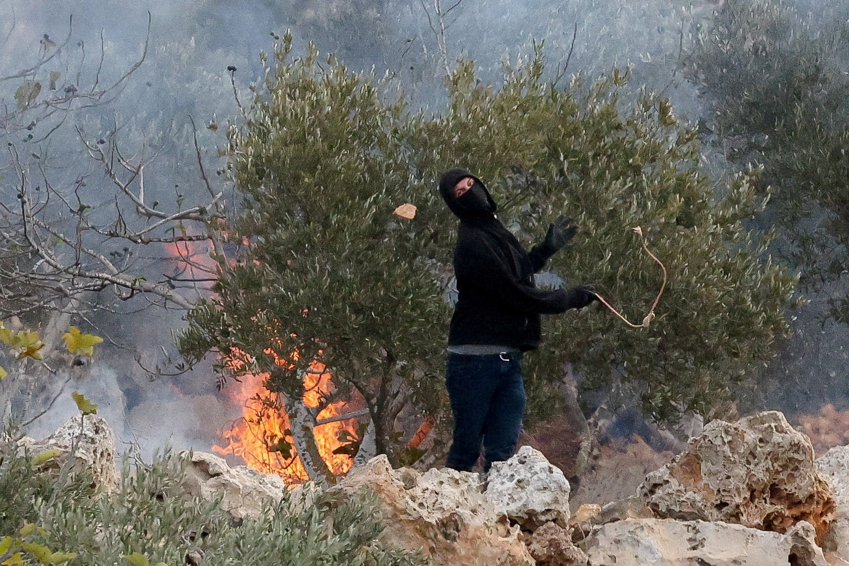 An Israeli settler hurls a stone toward Palestinians during clashes amid the olive harvest in Abu Falah, near Ramallah, occupied West Bank, Oct. 16, 2026. (Reuters/Ammar Awad/File Photo)