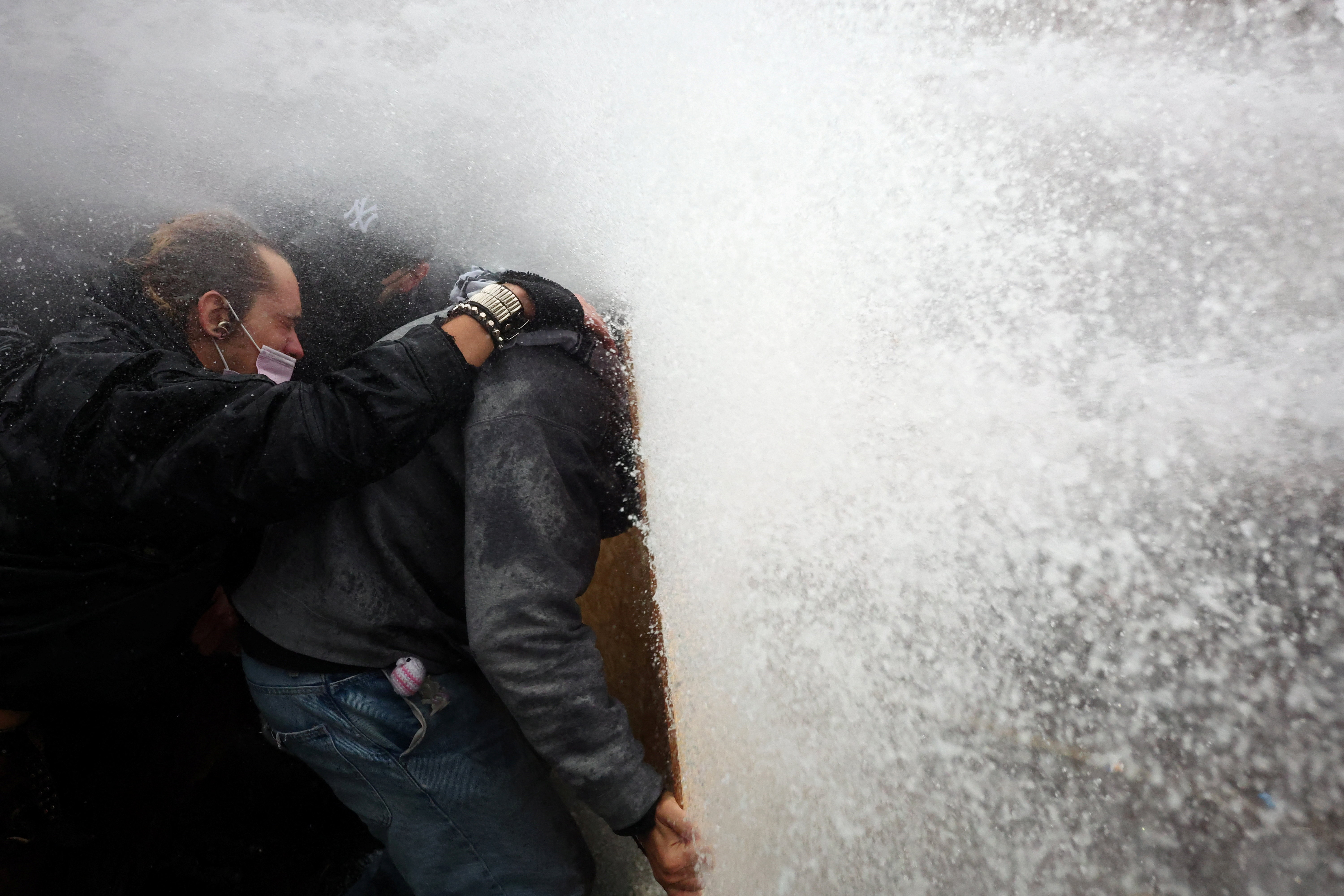 Protesters take cover behind a plywood board as French riot police use a water canon amid clashes during a demonstration in Paris on Saturday.