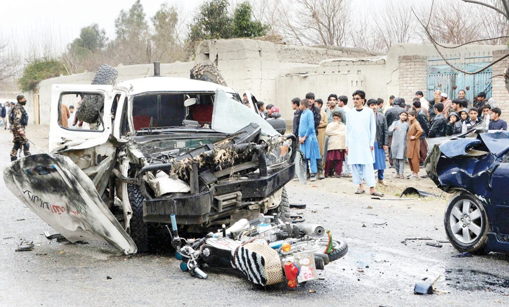 Afghan bystanders look on as security force personnel inspect wreckage of vehicles at the site of a roadside rickshaw bomb explosion that targeted a senior local police vehicle in Behsood district of Nangarhar province on Tuesday. (AFP)