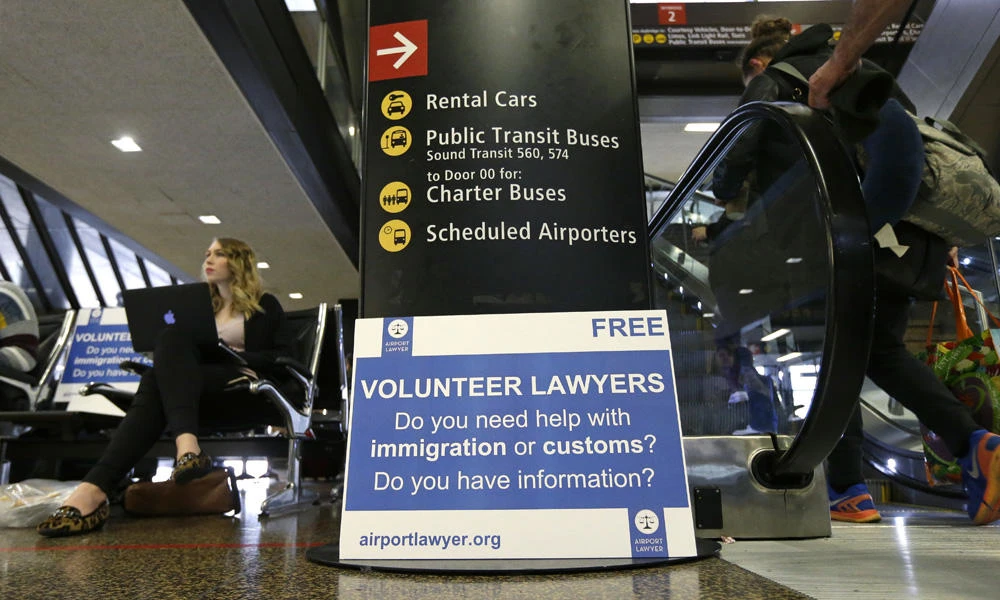 Asti Gallina, left, a volunteer law student from the University of Washington, sits at a station near where passengers arrive on international flights at Seattle-Tacoma International Airport on Tuesday in Seattle. Gallina was volunteering with the group Airport Lawyer, as airport officials and civil rights lawyers around the country are getting ready for President Donald Trump's new travel ban. (AP Photo/Ted S. Warren)