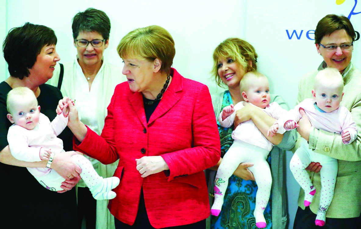 German Chancellor Angela Merkel grabs the hand of a triplet baby girl as she visits the Bosch Foundation to mark the 15th anniversary of the social organisation “wellcome” in Berlin on Monday. (Reuters)