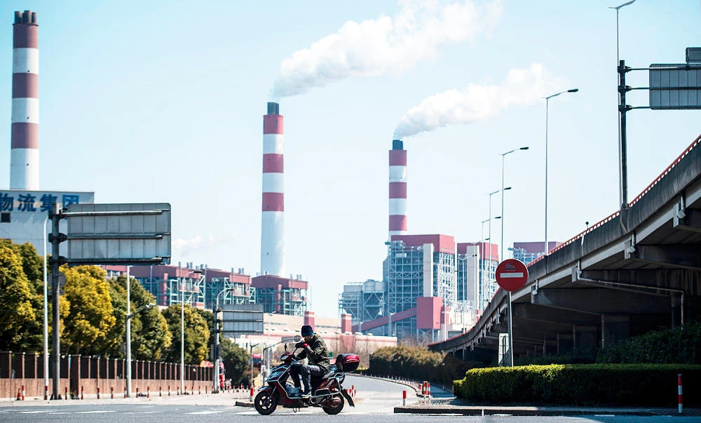 A man rides his scooter near the Shanghai Waigaoqiao Power Generator Company coal power plant in Shanghai on Monday. (AFP)