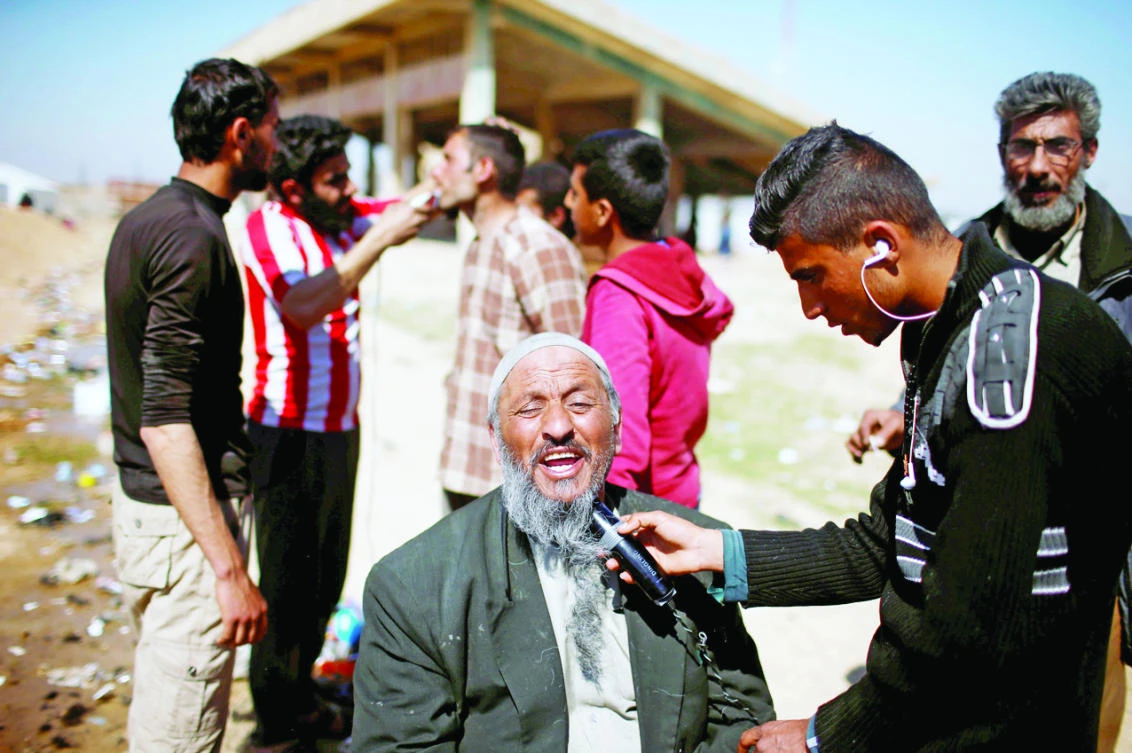 Displaced Iraqis who fled their homes have their beards shaved outside Hamam Al-Alil Camp, south of Mosul. (Reuters)