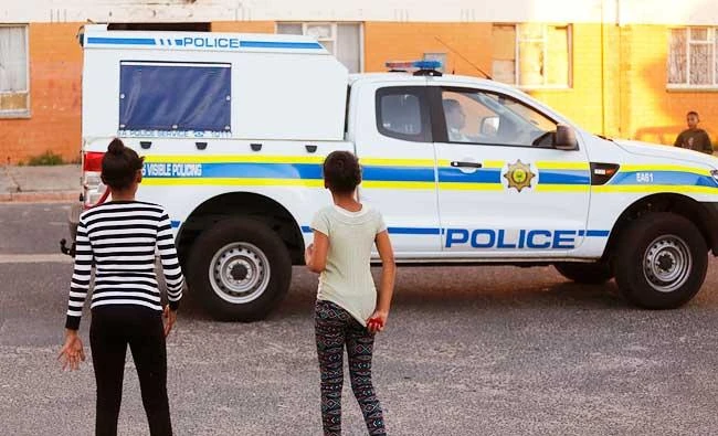 In this photo taken on May 6, 2016, two girls stand as a South African Police truck drives through Atlantis area on the outskirts of Cape Town, South Africa. (AP)