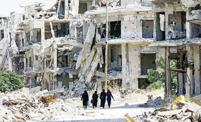 Syrian women walk between destroyed buildings in the regime-held Jouret Al-Shiah neighborhood of Homs. (AFP)