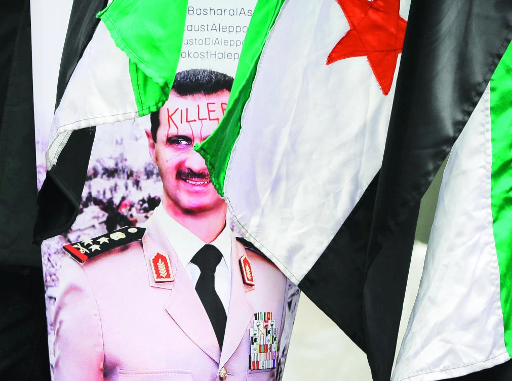 A poster of Syrian President Bashar Assad is displayed by members of the Syrian community protesting outside the Syrian Embassy in Bucharest on Friday. Syrians are marking the sixth anniversary of the civil war. (AP)