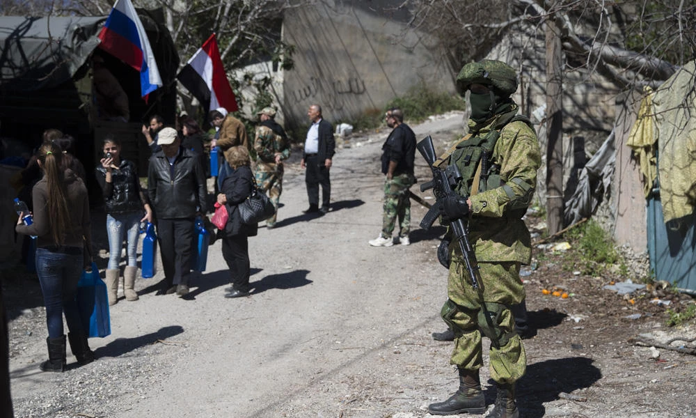 In this March 1, 2016, file photo, a Russian soldier keeps watch as local residents receive humanitarian aid in the Syrian village of Ghunaymiyah, about 15 kilometers from the Turkish border. (AP Photo/Pavel Golovkin, File)