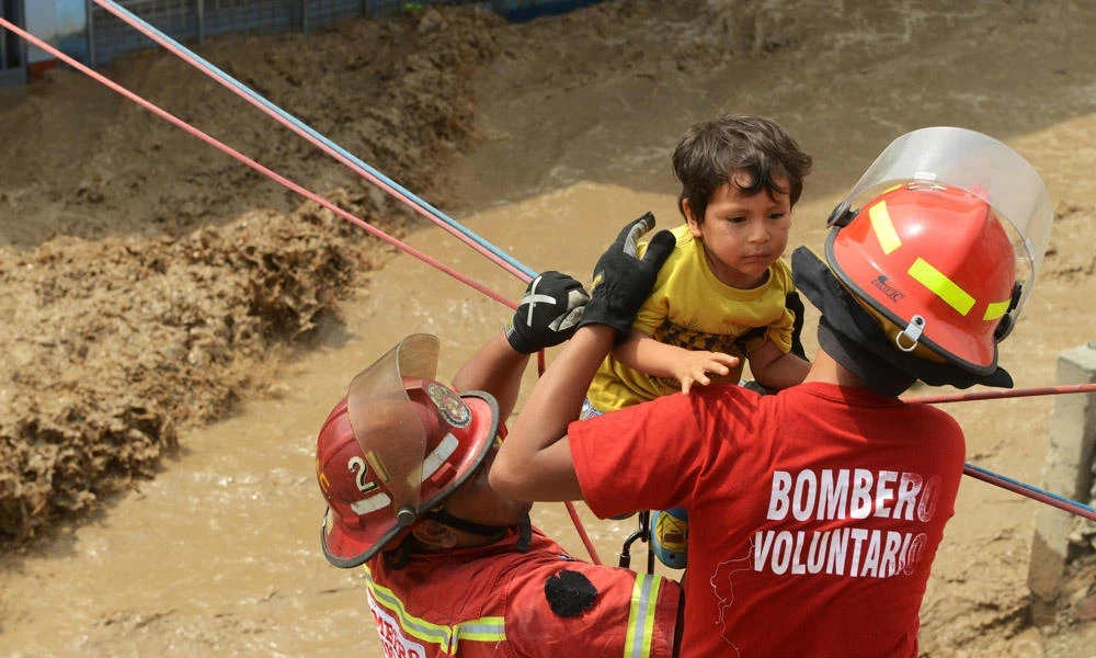 Residents of the Huachipa populous district, east of Lima, are helped on March 17, 2017, by police and firemen rescue teams to cross over flash floods hitting their neighborhood and isolating its residents. (AFP / CRIS BOURONCLE)