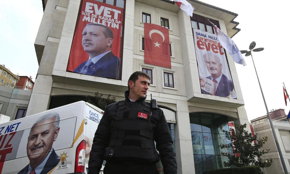 In this March 15, 2017 photo, a security guard stands outside the offices of the ruling Justice and Development Party (AKP) in Istanbul, decorated with posters of Turkey's President Recep Tayyip Erdogan and former AKP leader, top left, and Turkey's Prime Minister Binali Yildirim, top right, supporting the 'YES' vote ('Evet', in Turkish) for the upcoming referendum. (AP Photo/Lefteris Pitarakis)