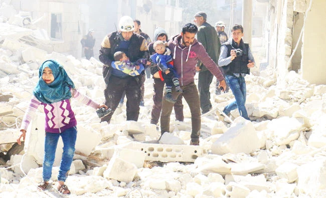 People and a civil defence personnel carry children at a damaged site after an air strike on rebel-held Idlib city, Syria on Sunday. (REUTERS)