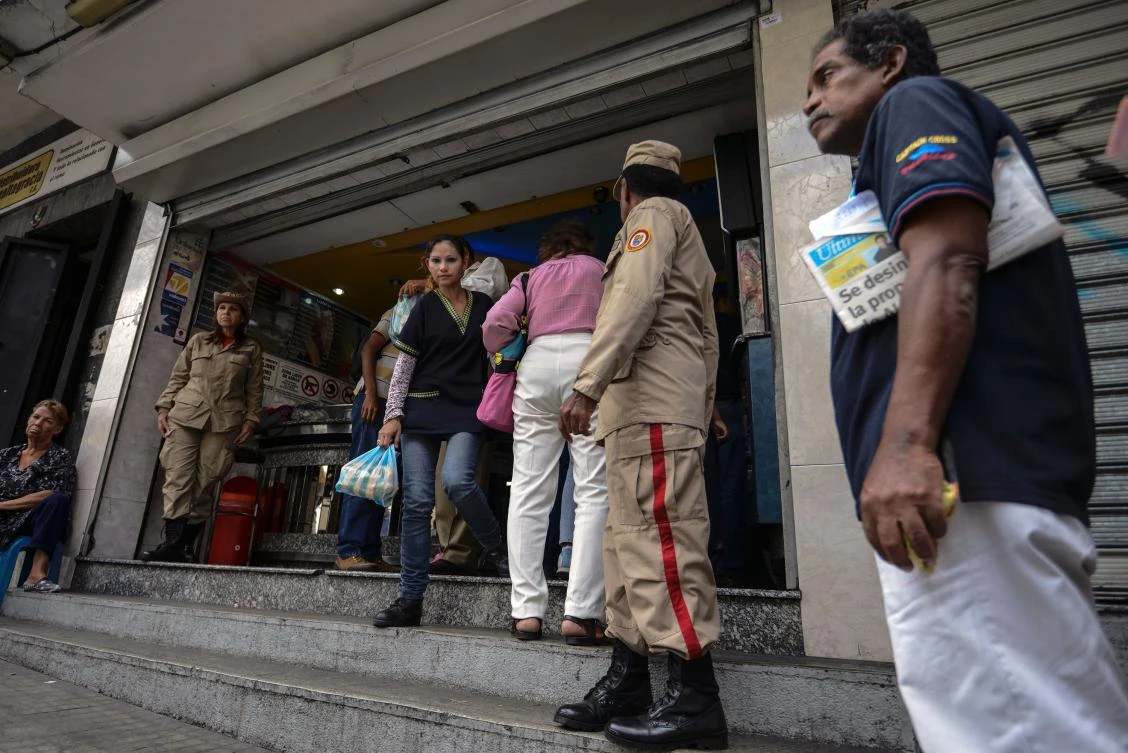 Members of the Bolivarian militia guard, as people queue to buy bread in a bakery in Caracas. (AFP)