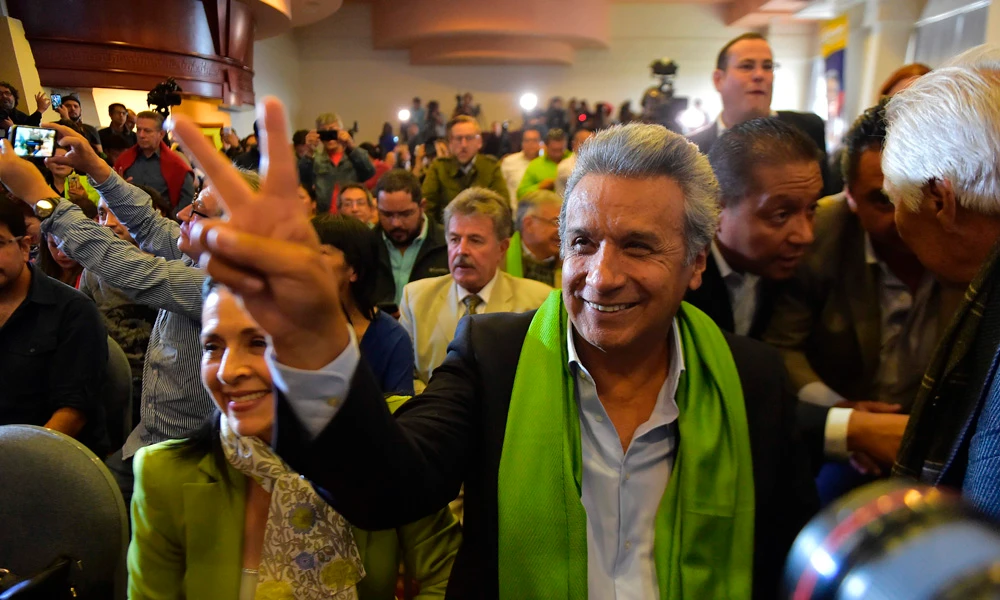 The Ecuadorean presidential candidate of the ruling Alianza PAIS party, Lenin Moreno, gives the "V for victory" sign next to his wife Rocio Gonzalez (L) as they listen with supporters to the first results of the runoff election, in Quito on April 2, 2017. (AFP / RODRIGO BUENDIA)