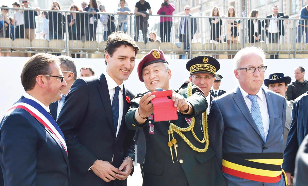 Canadian Prime Minister Justin Trudeau, flanked by Arras Mayor Frederic Leturque, poses for a selfie picture with a veteran at the Heroes Square in Arras during a ceremony to commemorate the 100th anniversary of the Battle of Vimy Ridge. (AFP)