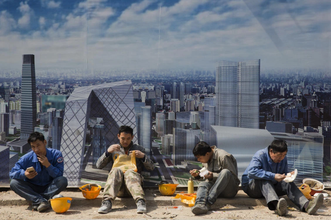 Construction workers eat lunch in front of an artist's impression of the Central Business District in Beijing, China. (AP)