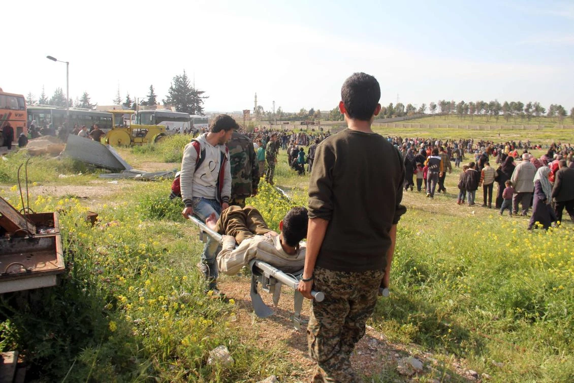 A wounded Syrian, evacuated from two besieged government-held towns of Fuaa and Kafraya, is carried into a field near the site of a suicide car bombing that targeted their buses in Rashidin, west of Aleppo, on April 15, 2017. (AFP)