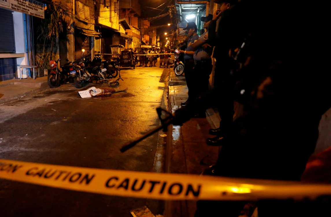Policemen stand guard near the body of a man killed during what police said was a drug related vigilante killing Manila, Philippines. (Reuters)