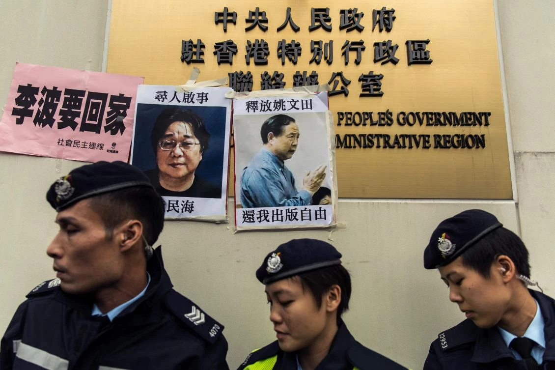 In this file photograph taken on January 3, 2016, police walk past missing person notices of Gui Minhai (L) posted on top of the sign of China's Liaison Office in Hong Kong. Gui Minhai, a Chinese-born scholar and book publisher has been honoured by a Swedish press rights group for his struggle for freedom of speech in his native country. (AFP / ANTHONY WALLACE)