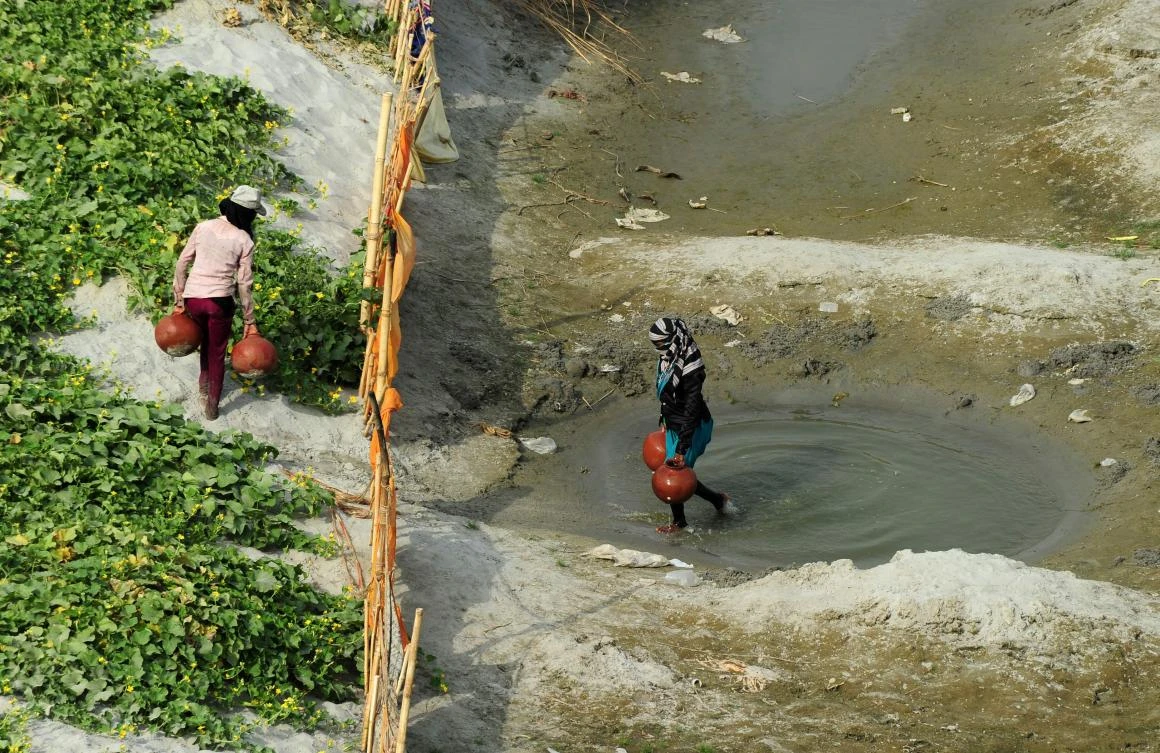 Indian farmers collect water from a temporary pond to irrigate their cucumber farm near a river bed area of the River Ganges in Allahabad on Friday. (AFP / Sanjay Kanojia)