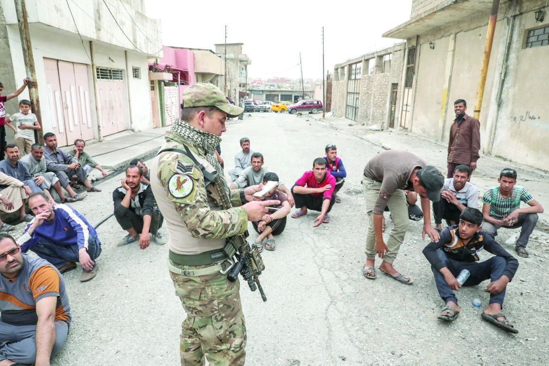 Displaced Iraqi men wait for a security check on a street near western Mosul. (Reuters)