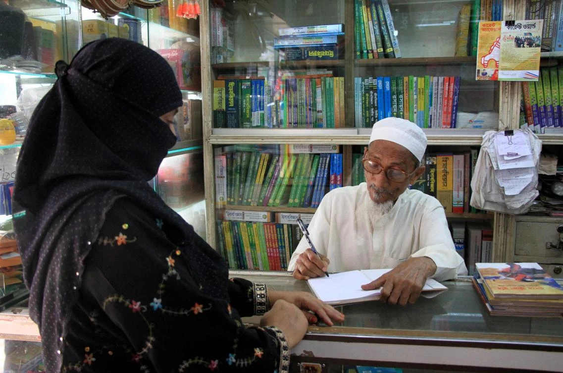Bangladeshi novelist Kasem bin Abubakar signs an autograph for a relative at his book shop in Dhaka. (AFP)