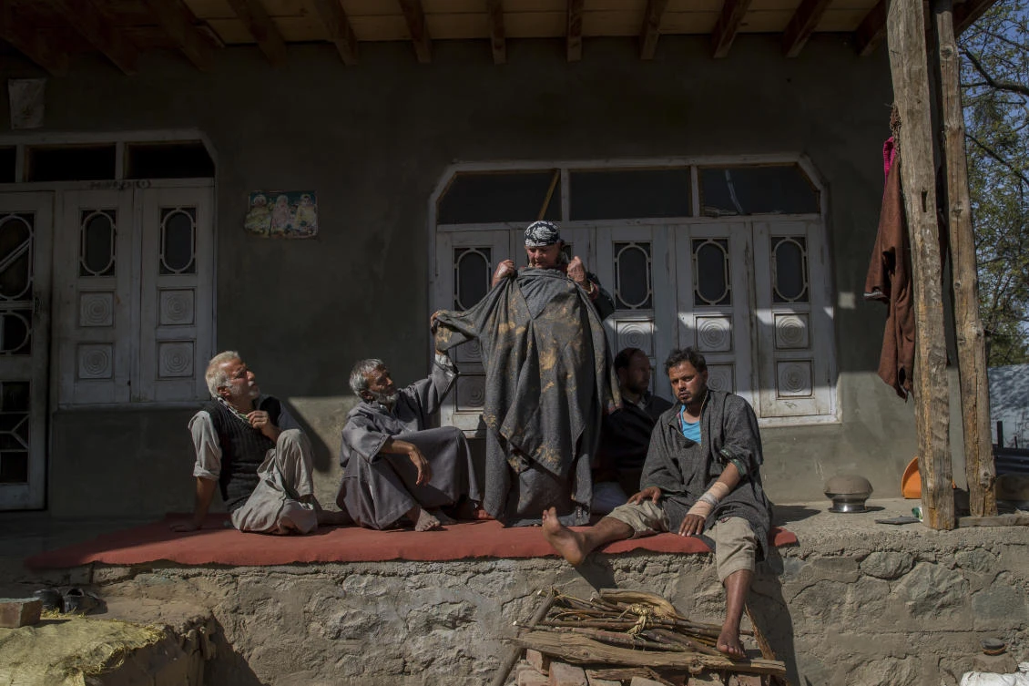 Kashmiri man Farooq Ahmed Dar, right, sits as his mother displays a muddy and torn out robe that Dar was wearing on the day of his alleged abuse at his residence in Chill village.(AP Photo)