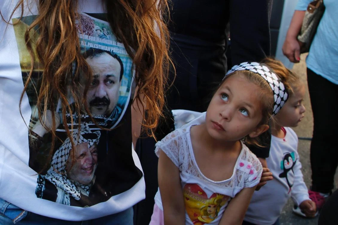 A Palestinian girl looks up at a woman wearing a t-shirt bearing portraits of late palestinian leader Yasser Arafat (bottom) and Palestinian leader and prominent prisoner Marwan Barghouti during a demonstration in the West Bank city of Ramallah in support of Barghouti and other prisoners on hunger strike in Israeli jails on April 24, 2017. Barghouti's health has declined seriously over the past week after he joined a hunger strike with more than 1,000 other prisoners in Israel, an NGO said Monday. (AFP)