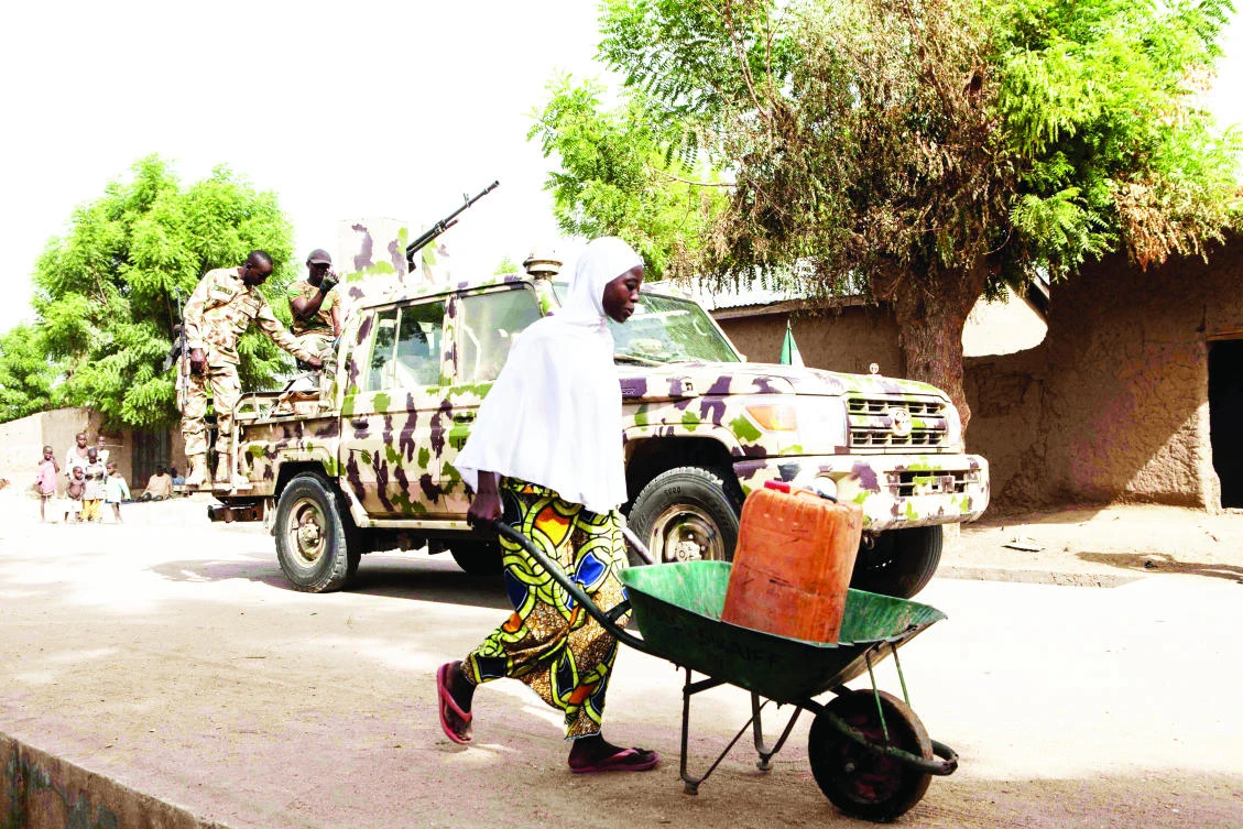 A woman pushes a wheelbarrow as Nigerian soldiers patrol in Banki, Nigeria. (AFP)