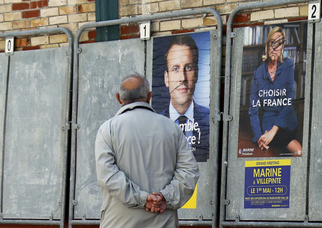 A man walks past defaced election campaign posters for French centrist presidential candidate Emmanuel Macron and far-right candidate Marine Le Pen, in Saint Jean de Luz, southwestern France, on Thursday. (AP)