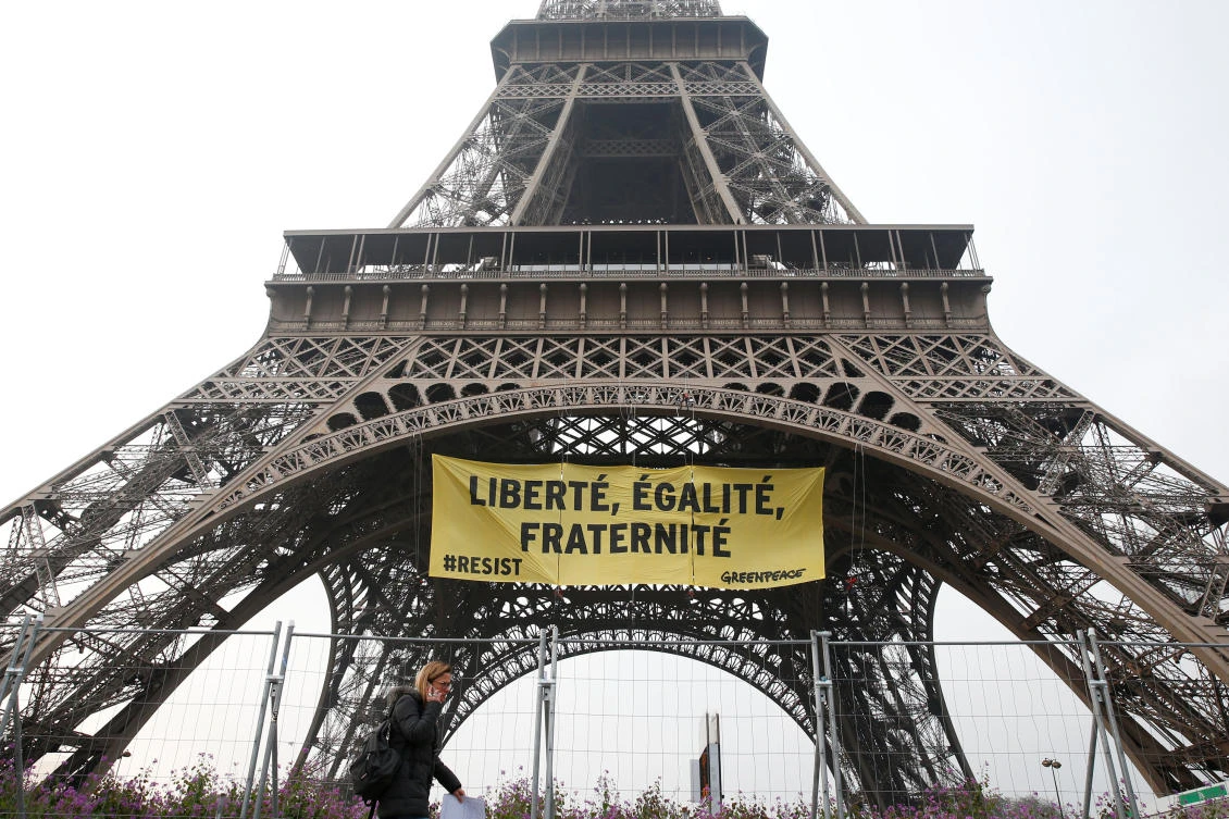 A woman passes by as activists from the environmentalist group Greenpeace unfurl a giant banner on the Eiffel Tower which reads "Liberty, Equality, Fraternity" in a call on French citizens to vote against the National Front (FN) presidential candidate Marine Le Pen, in Paris, France May 5, 2017. (REUTERS)