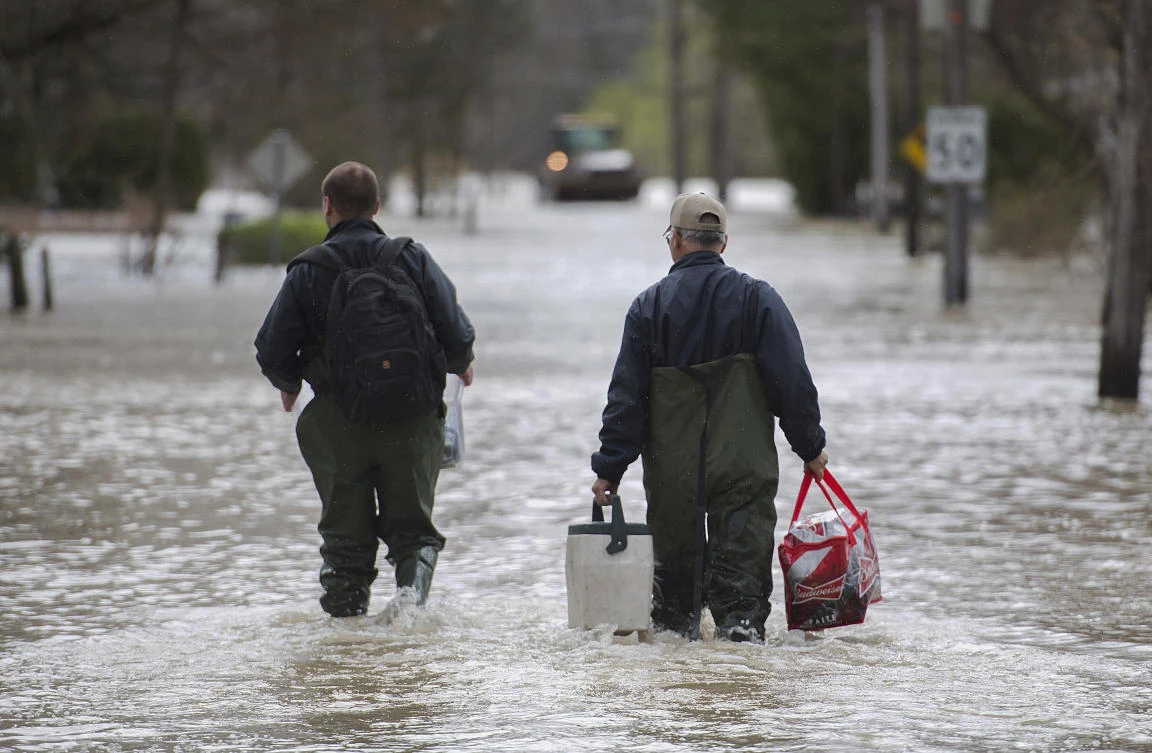 Two men carry belongings along a flooded street in the town of Rigaud west of Montreal, Sunday, May 7, 2017, following flooding in the region. (Graham Hughes/The Canadian Press via AP)