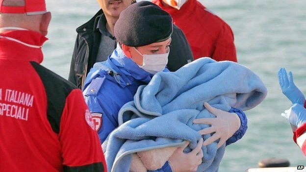 A Red Cross volunteer carries a baby wrapped in a blanket after migrants disembarked at the Sicilian Porto Empedocle harbour. (AP)