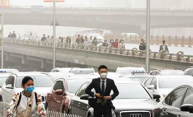 People wearing face masks walk past cars clogged with heavy traffic on a road as Beijing is hit by polluted air and sandstorm, in this May 4, 2017 photo. (AP)