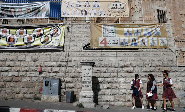Palestinian schoolgirls walk past campaign posters displaying electoral lists ahead of municipal elections in the West Bank city of Bethlehem. (AFP / THOMAS COEX)