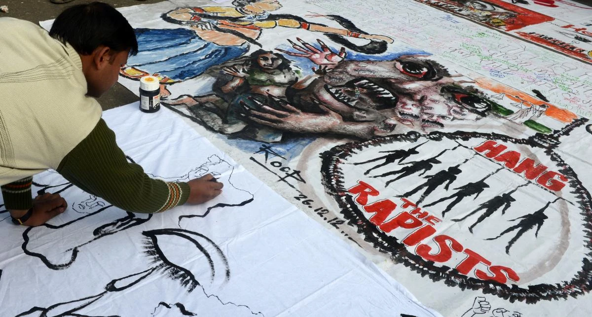 (FILES) This file photograph taken on December 30, 2012, shows an Indian bystander writing on a banner featuring images of 'government and rapists' as it lies on a road in New Delhi, after the cremation ceremony for a gangrape victim. India's Supreme Court on May 5, 2017, has upheld the death sentences of four men convicted in the 2012 gang rape and murder of a Delhi student. (AFP)