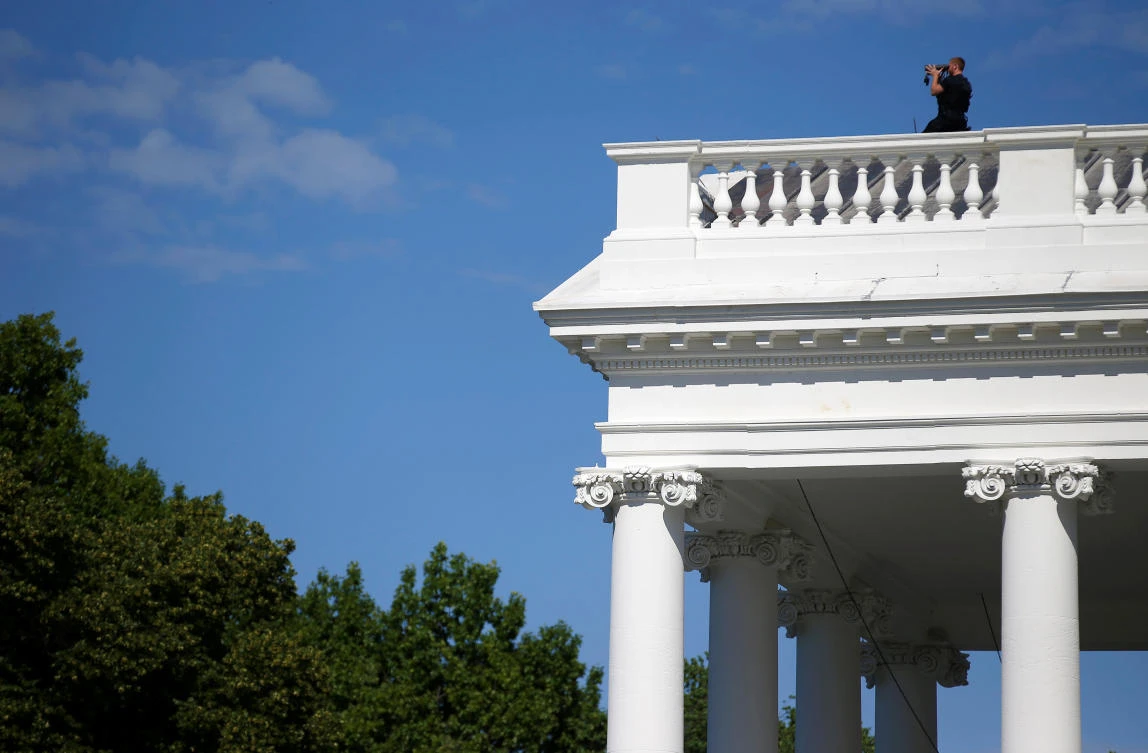 A Secret Service officer looks out from the roof of the North Portico in reaction to an apparent fence jumper at the White House. (Reuters)