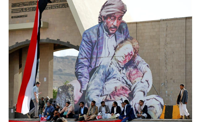 Houthi followers sit under a picture of a man holding a child supposedly killed by a recent Arab coalition air strike at the site of a demonstration in Sanaa, Yemen, on May 20, 2017. (REUTERS/Khaled Abdullah)
