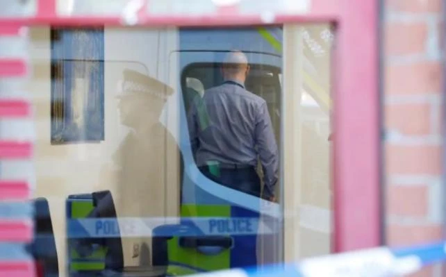 A police officer is reflected in the window of a barber's shop in Moss Side as plain clothes officers search inside. (REUTERS)