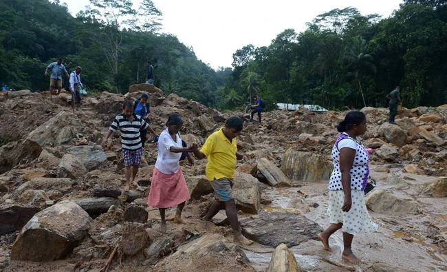 Sri Lankan villagers cross a landslide site as military rescue workers and villagers search for survivors in Athweltota village in Kalutara on Sunday. (AFP / LAKRUWAN WANNIARACHCHI)