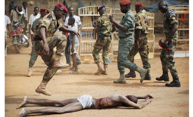 In this Feb. 5, 2014 photo, a FACA (Central African Armed Forces) officer jumps on the lifeless body of a suspected Muslim Seleka militiaman moments after Central African Republic Interim President Catherine Samba-Panza addressed the troops in Bangui, Central African Republic. A sweeping United Nations report has identified hundreds of human rights violations in Central African Republic that may amount to war crimes.(AP Photo/Jerome Delay-File)