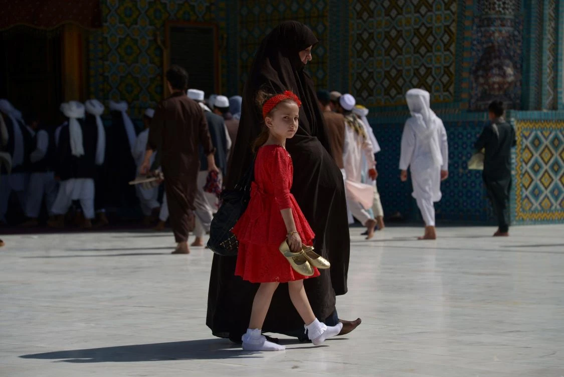 An Afghan girl walks with her mother through the courtyard of Hazrat Ali shrine, or Blue Mosque, during Eid al-Fitr prayers in Mazar-i-Sharif on June 25, 2017. / AFP / Farshad USYAN