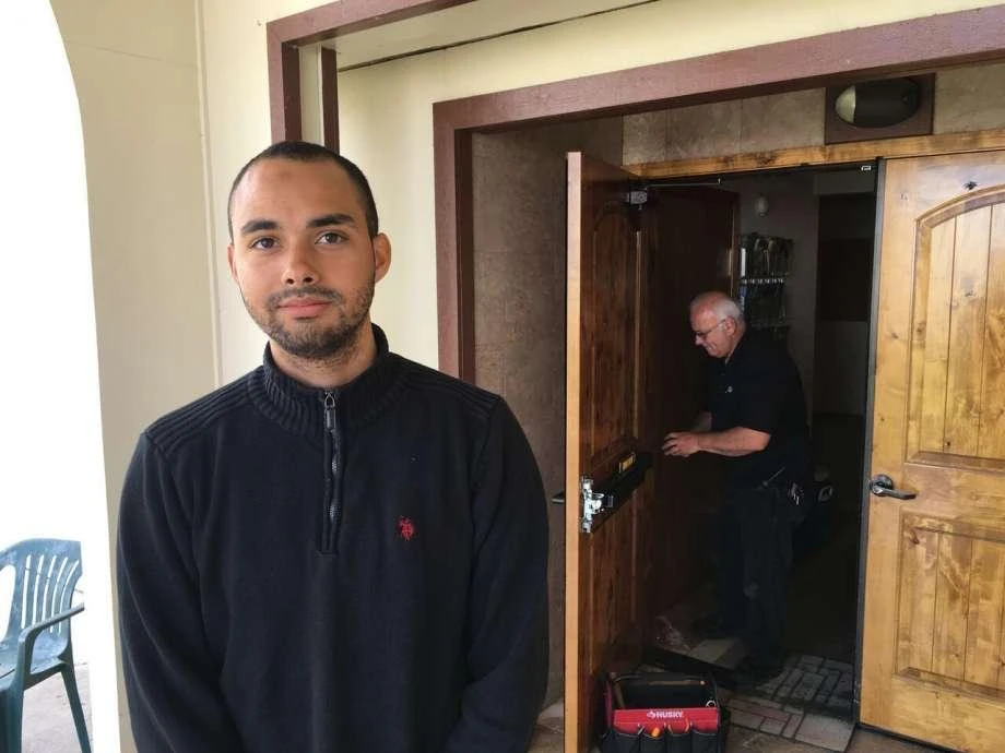 Drew Williams, a member of the Eugene Islamic Center, poses for a portrait outside the building in Eugene, Ore., as locksmith Jim King upgrades the locks on the front doors. (AFP)